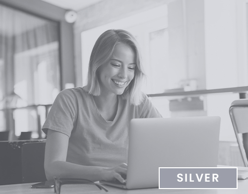A person smiling while using a laptop indoors, with "SILVER" text overlay on the image. Background appears to show modern interior elements.